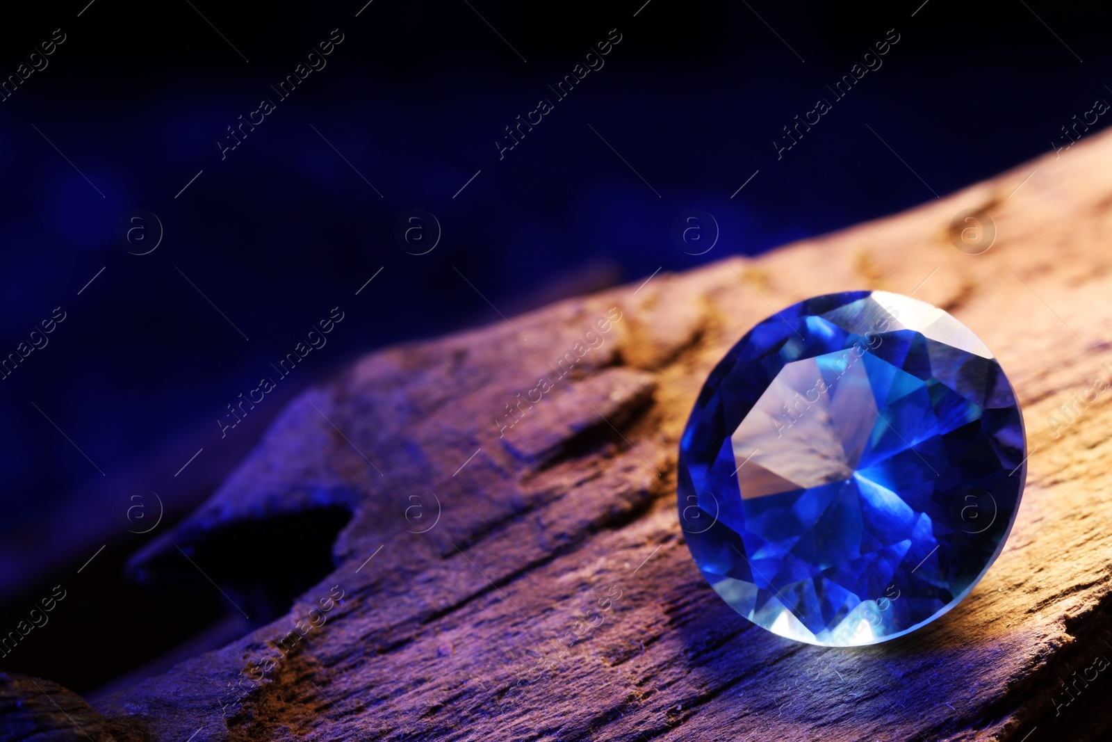 Photo of Beautiful shiny light blue gemstone on stone against dark background, closeup