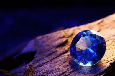 Photo of Beautiful shiny light blue gemstone on stone against dark background, closeup