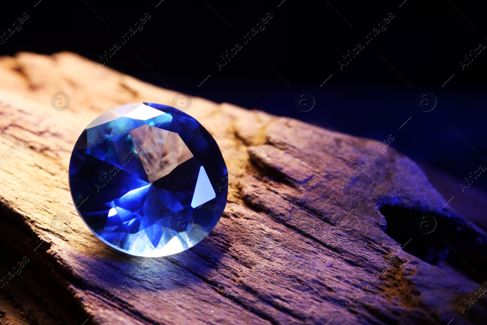 Photo of Beautiful shiny light blue gemstone on stone against dark background, closeup