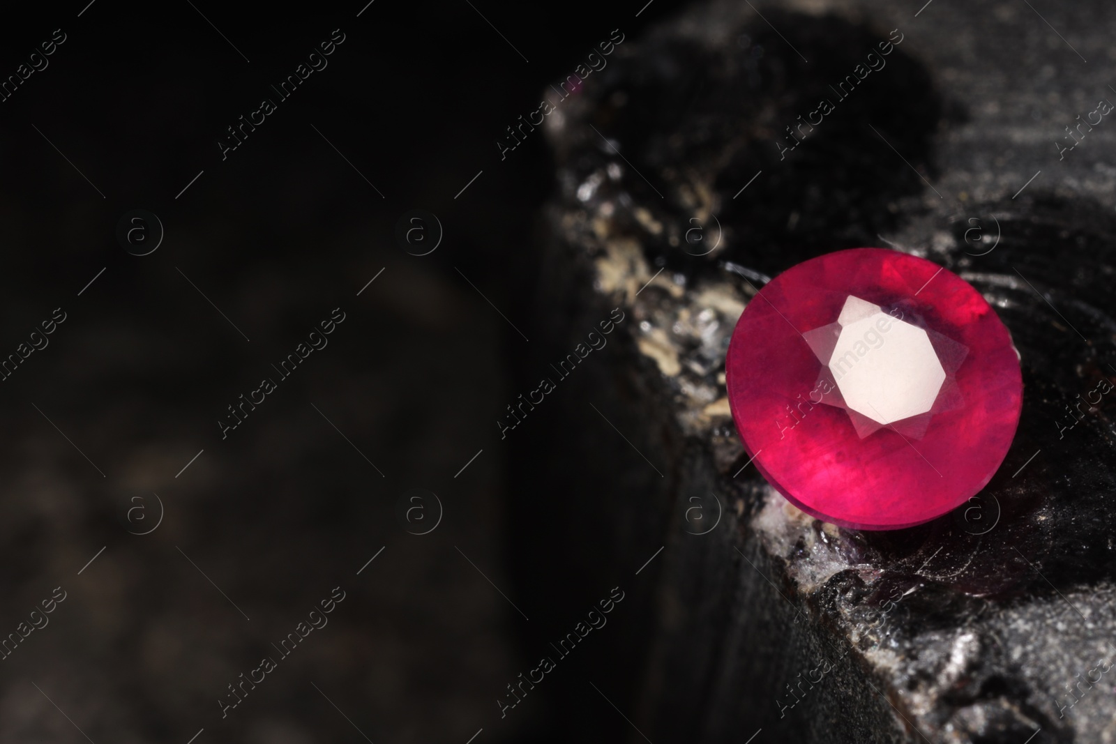 Photo of Beautiful shiny pink gemstone on stone, space for text