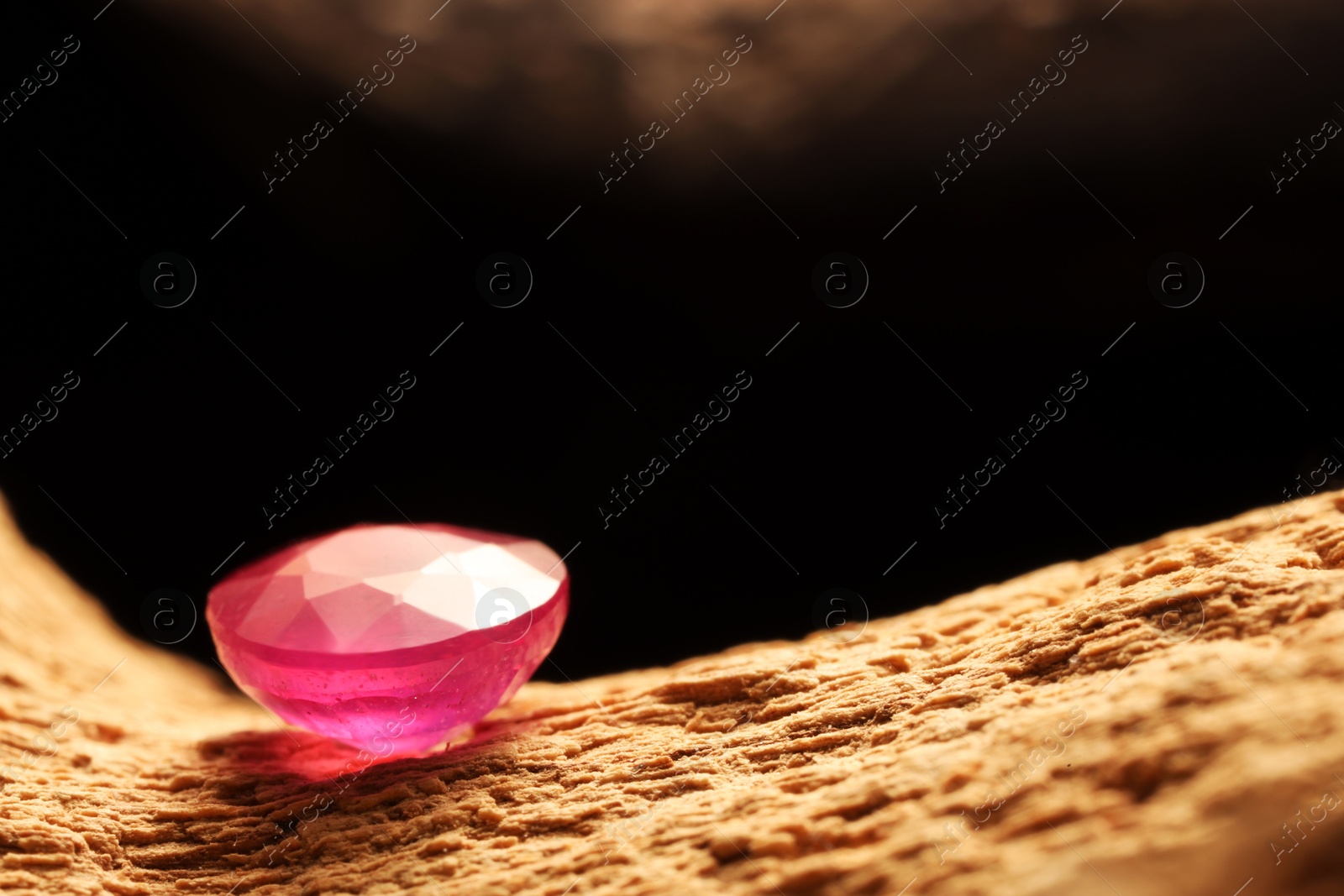 Photo of Beautiful shiny pink gemstone on stone against dark background, closeup. Space for text