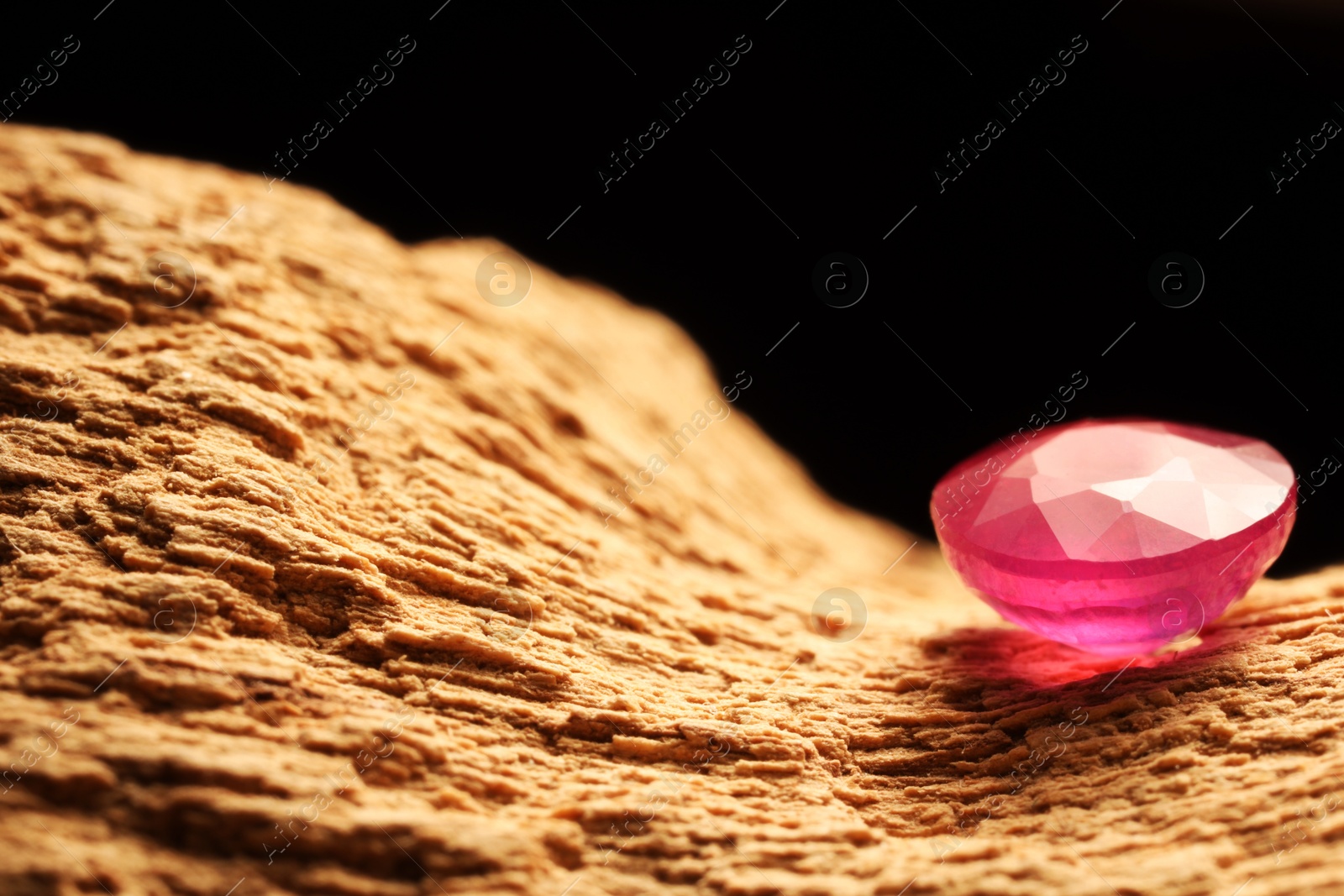 Photo of Beautiful shiny pink gemstone on stone against dark background, closeup. Space for text