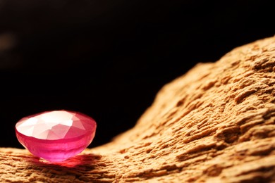 Photo of Beautiful shiny pink gemstone on stone against dark background, closeup. Space for text