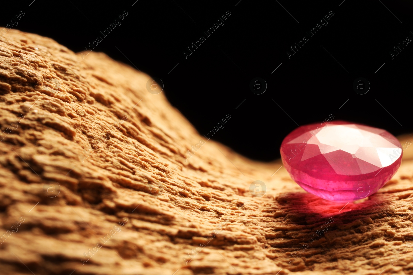 Photo of Beautiful shiny pink gemstone on stone against dark background, closeup. Space for text