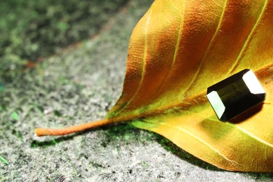 Photo of Shiny green gemstone and dry leaf on stone, closeup