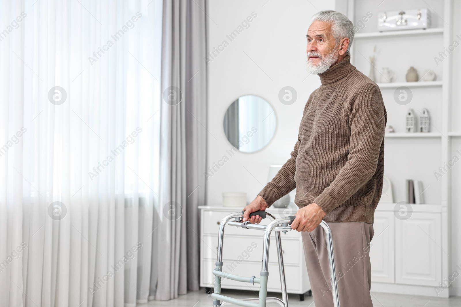 Photo of Senior man using walking frame at home. Space for text