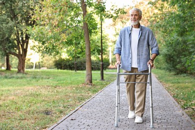 Photo of Senior man with walking frame in park, space for text