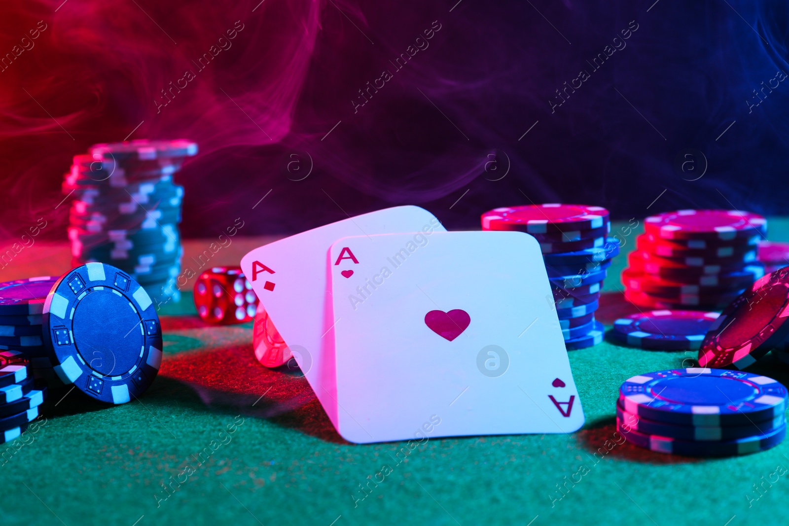 Photo of Poker chips and playing cards on green table in neon lights, closeup