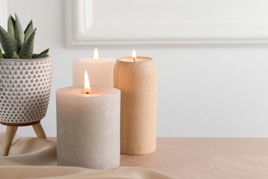 Photo of Beautiful burning candles, houseplant and cloth on wooden table, closeup. Space for text