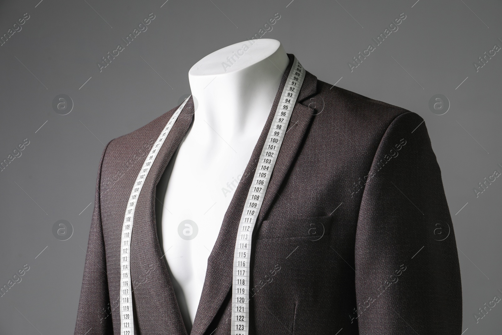 Photo of Male mannequin with brown jacket and measuring tape on grey background, closeup