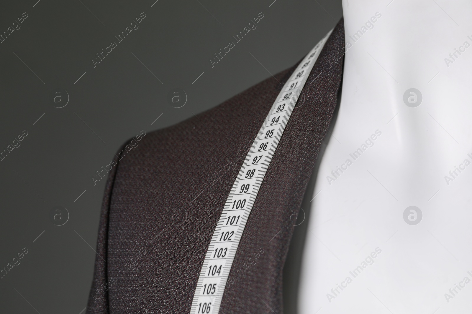 Photo of Male mannequin with brown jacket and measuring tape on grey background, closeup