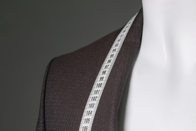 Photo of Male mannequin with brown jacket and measuring tape on grey background, closeup