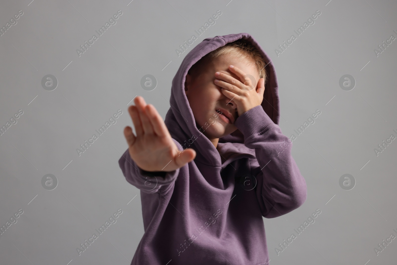 Photo of Scared little boy covering face with hand on grey background