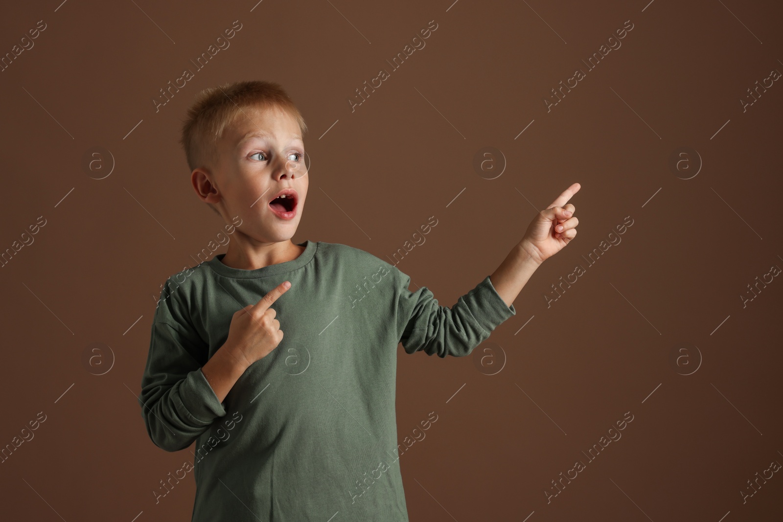 Photo of Scared little boy pointing at something on brown background. Space for text