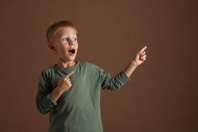 Photo of Scared little boy pointing at something on brown background. Space for text