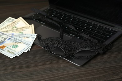 Photo of Sex work. Laptop, mask and money on wooden surface, closeup