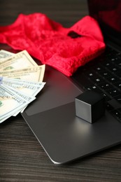 Photo of Sex work. Laptop, lingerie, dice and money on wooden surface, closeup