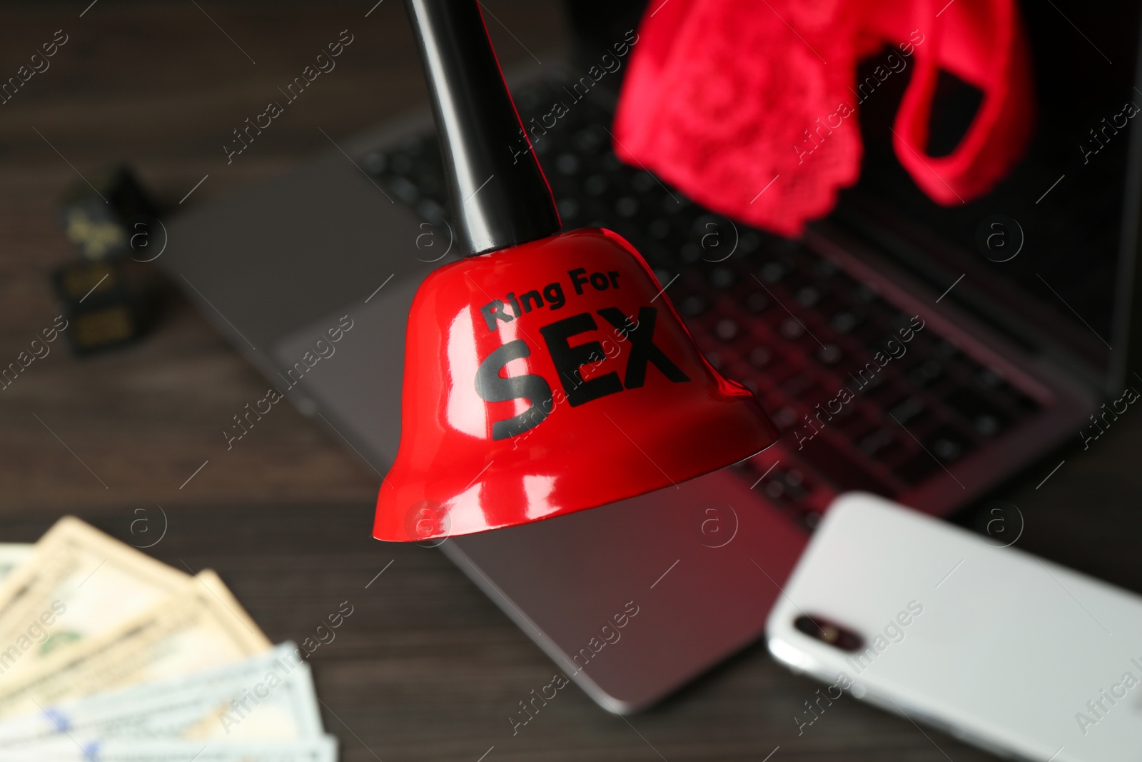 Photo of Sex work. Bell with phrase Ring for sex, laptop, lingerie, smartphone, dice and money on wooden surface, selective focus