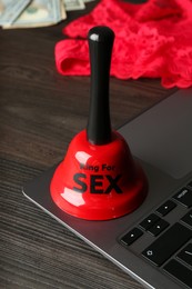 Photo of Sex work. Laptop, lingerie, bell and money on wooden surface, closeup