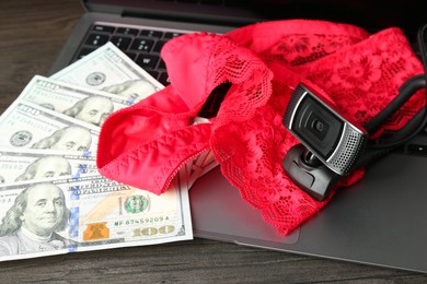 Photo of Sex work. Laptop with web camera, panties and money on wooden surface, closeup