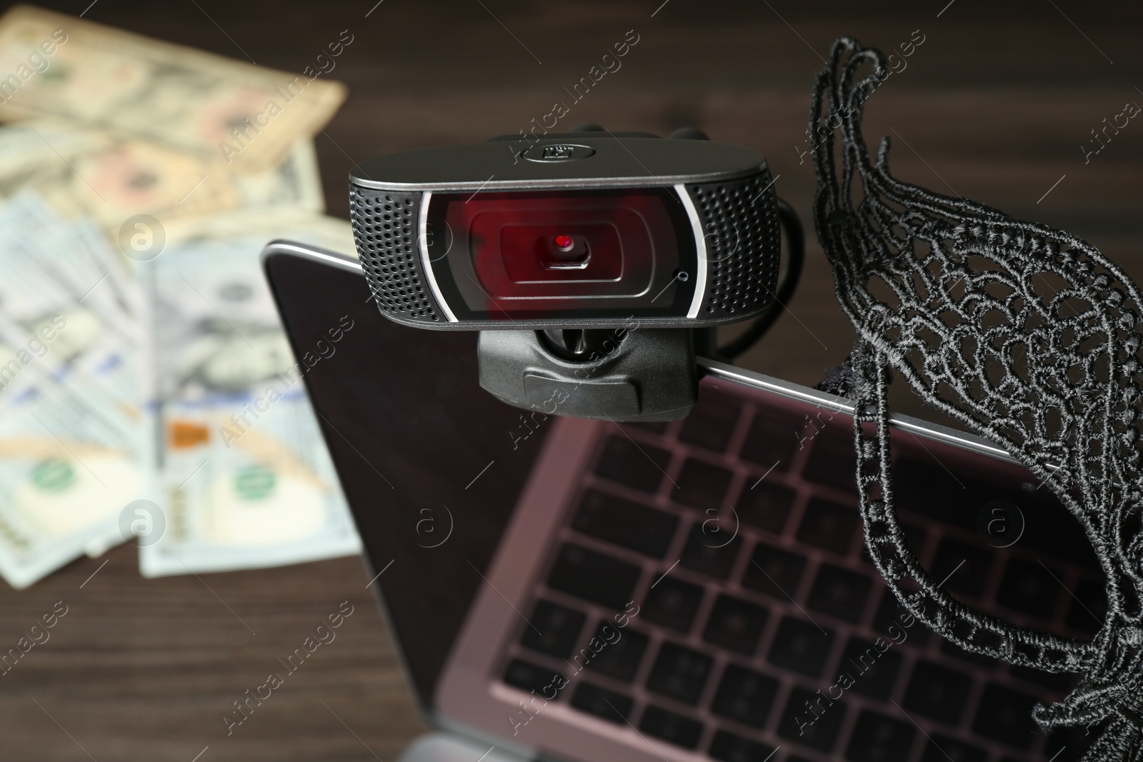 Photo of Sex work. Laptop with web camera and mask on wooden surface, closeup