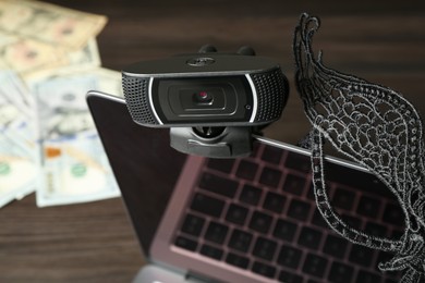 Photo of Sex work. Laptop with web camera and mask on wooden surface, closeup