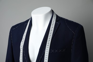 Photo of Semi-ready jacket with tailor's measuring tape on mannequin against grey background, closeup