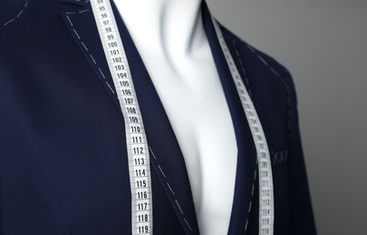 Photo of Semi-ready jacket with tailor's measuring tape on mannequin against grey background, closeup