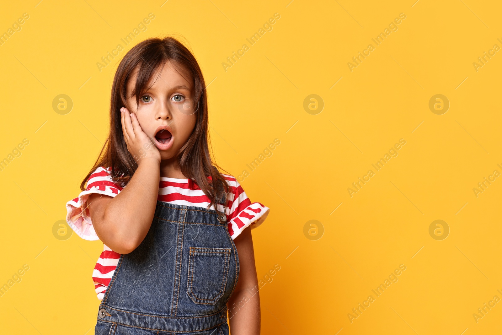 Photo of Portrait of scared little girl on orange background. Space for text