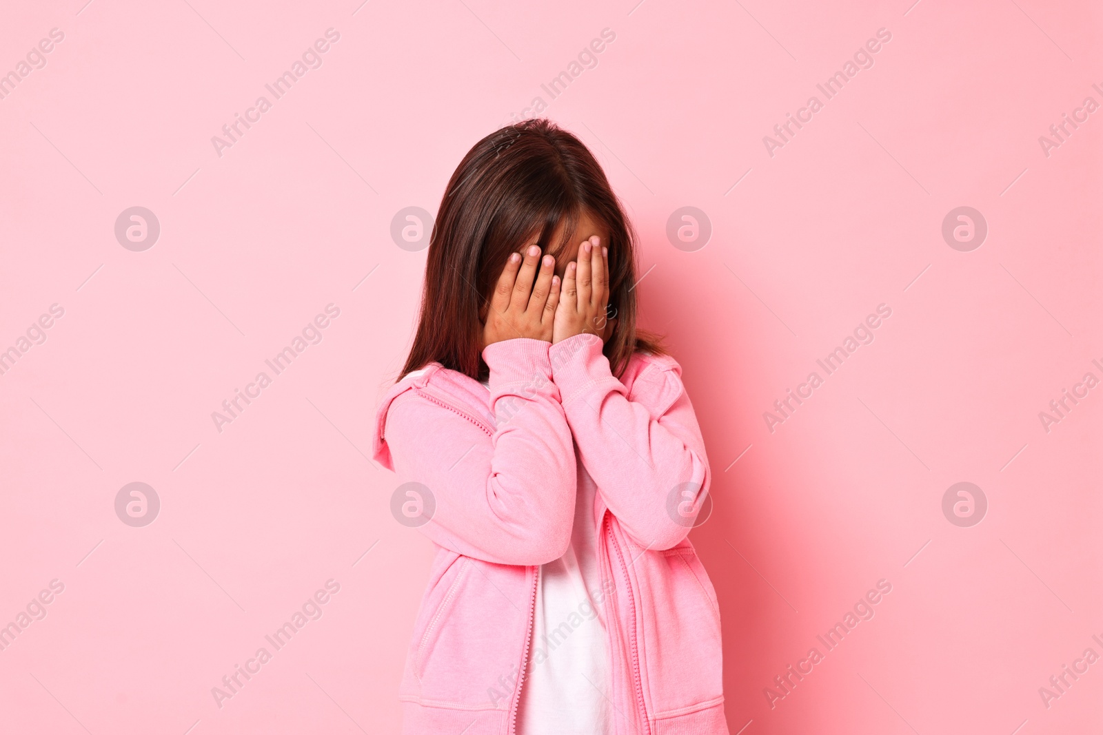 Photo of Scared little girl covering face with hands on pink background