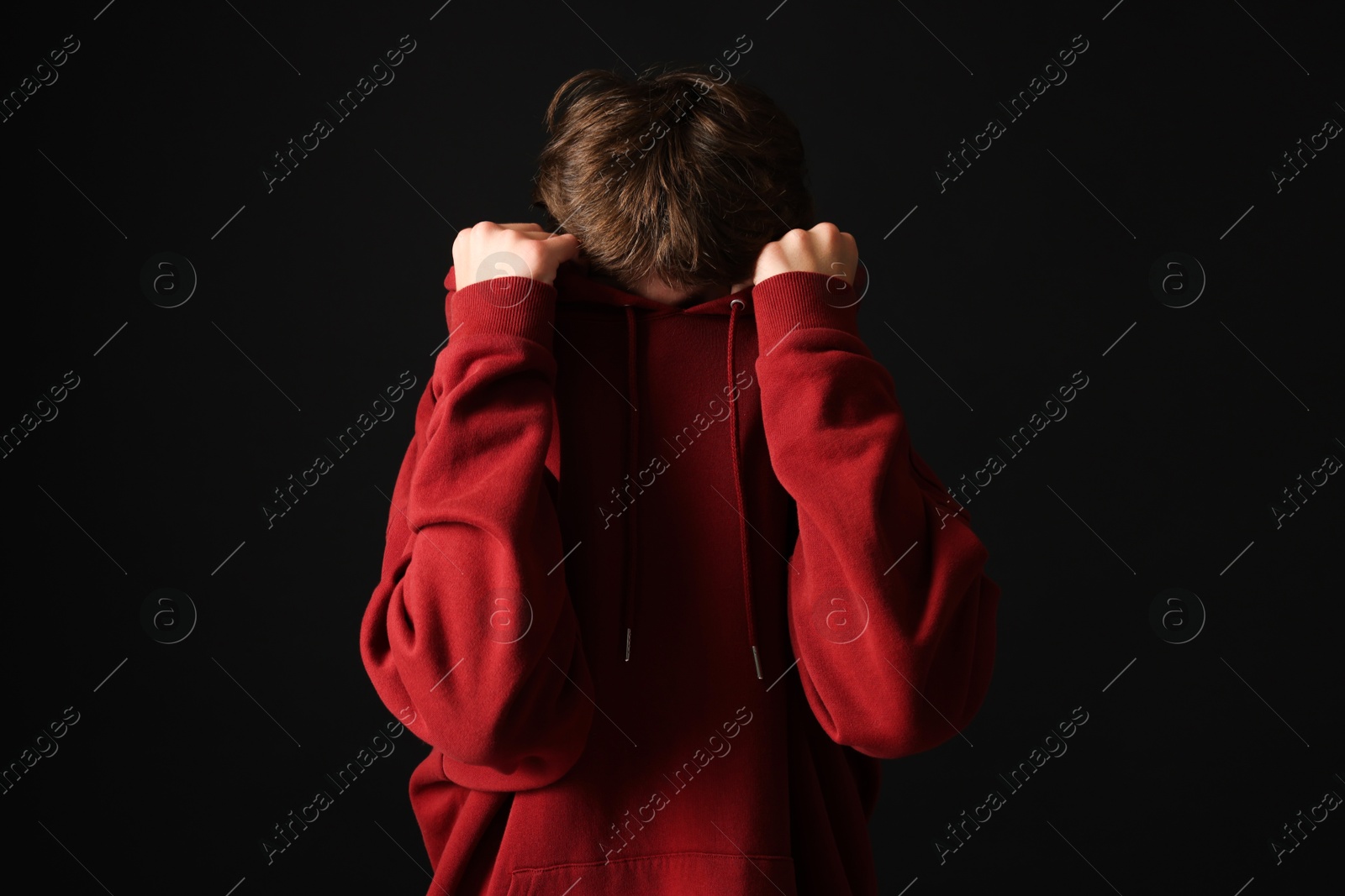 Photo of Scared teenage boy hiding on black background