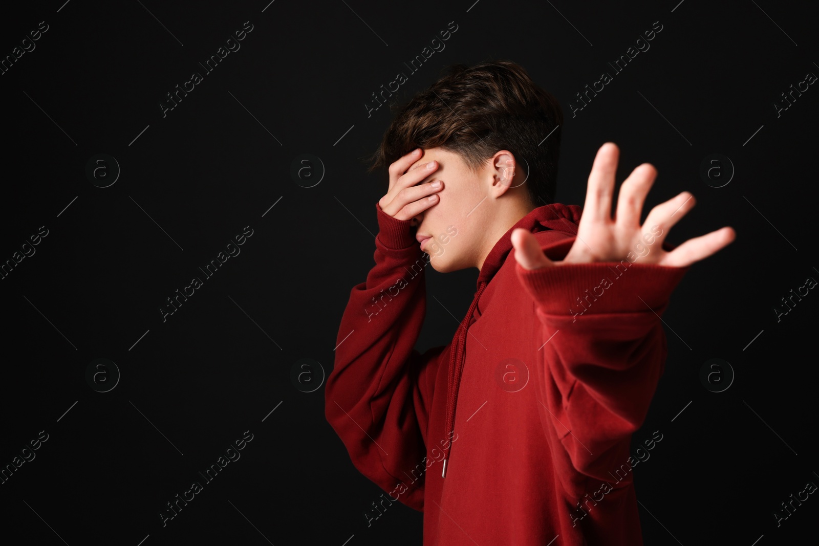 Photo of Scared teenage boy covering face with hands on black background. Space for text