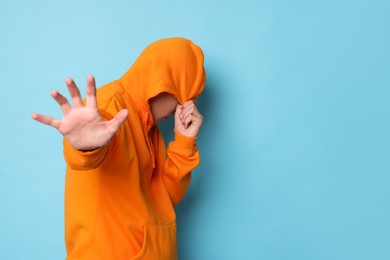 Photo of Scared teenage boy hiding on light blue background. Space for text