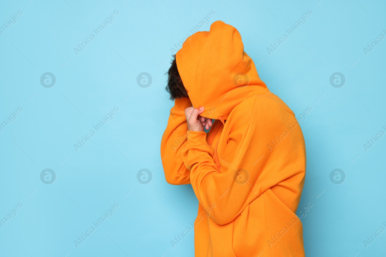 Photo of Scared teenage boy hiding on light blue background. Space for text