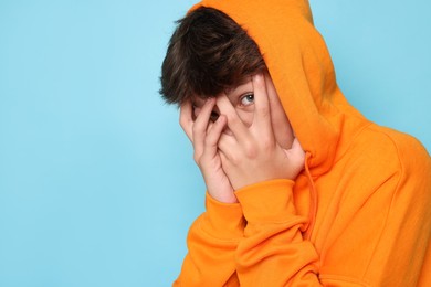 Photo of Scared teenage boy covering face with hands on light blue background. Space for text