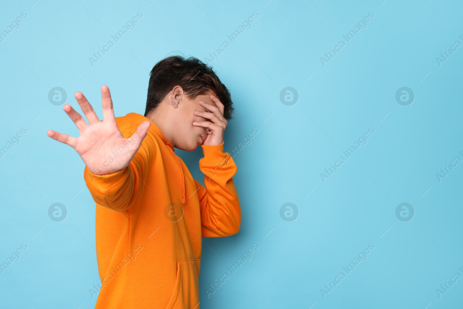 Photo of Scared teenage boy covering face with hand on light blue background. Space for text