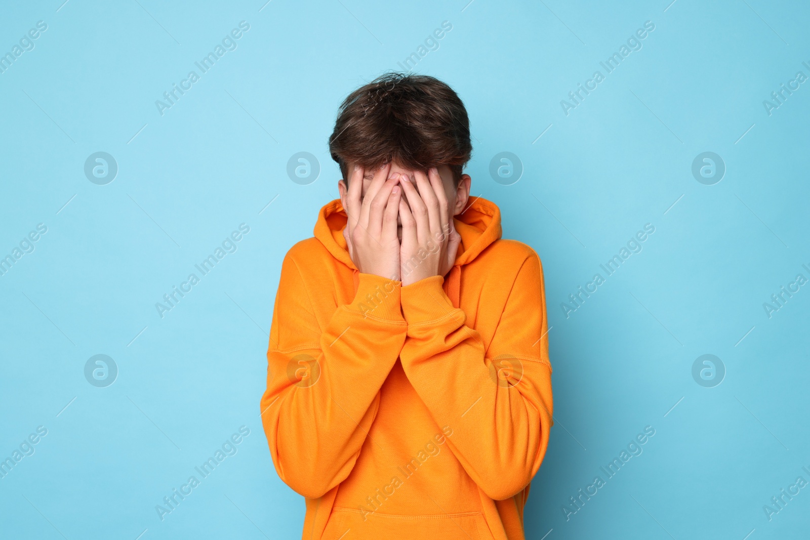 Photo of Scared teenage boy covering face with hands on light blue background