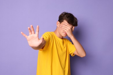 Photo of Scared teenage boy covering face with hand on violet background