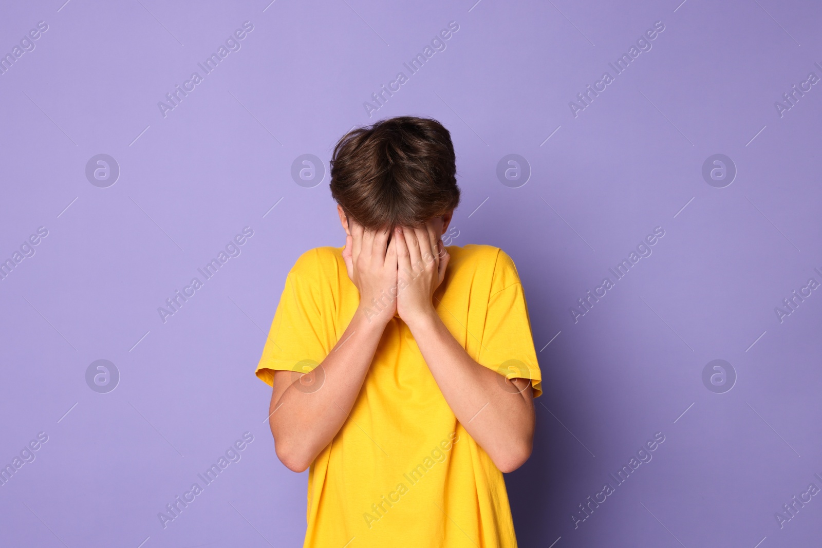 Photo of Scared teenage boy covering face with hands on violet background