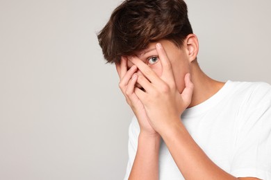 Photo of Scared teenage boy covering face with hands on grey background. Space for text