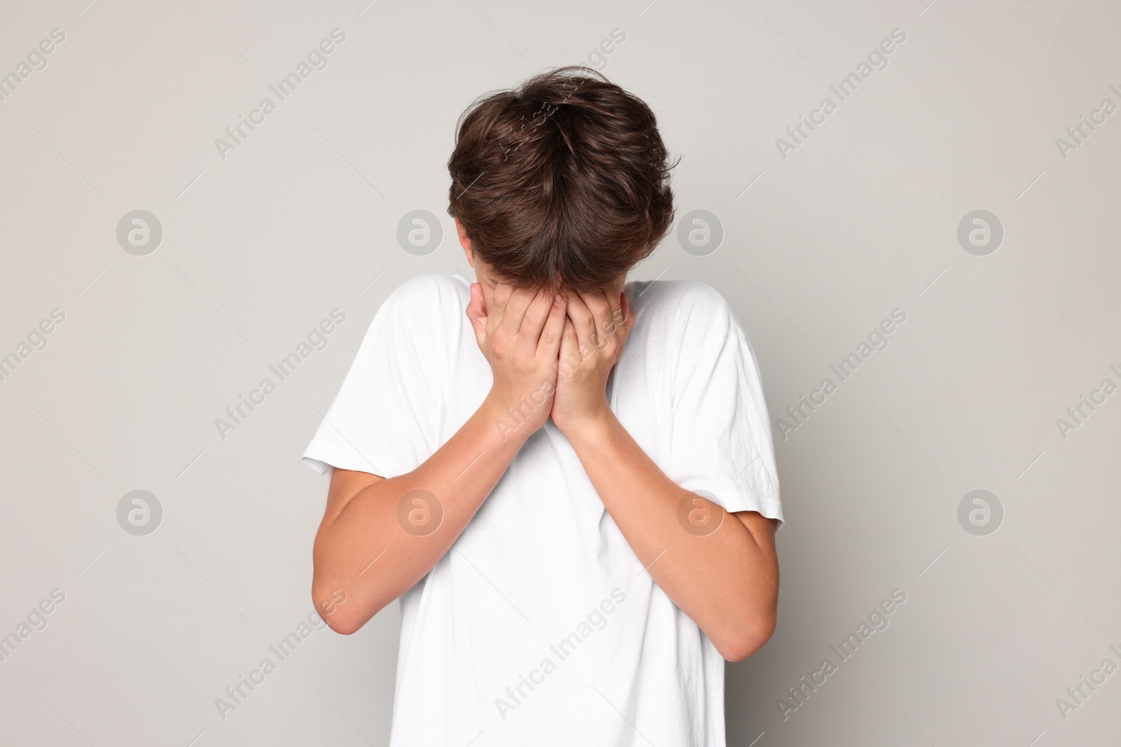 Photo of Scared teenage boy covering face with hands on grey background