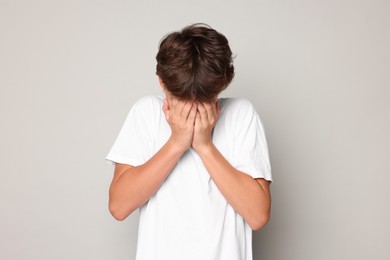 Photo of Scared teenage boy covering face with hands on grey background