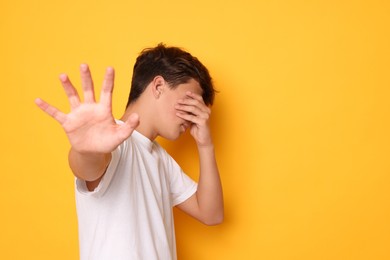 Photo of Scared teenage boy covering face with hand on orange background. Space for text