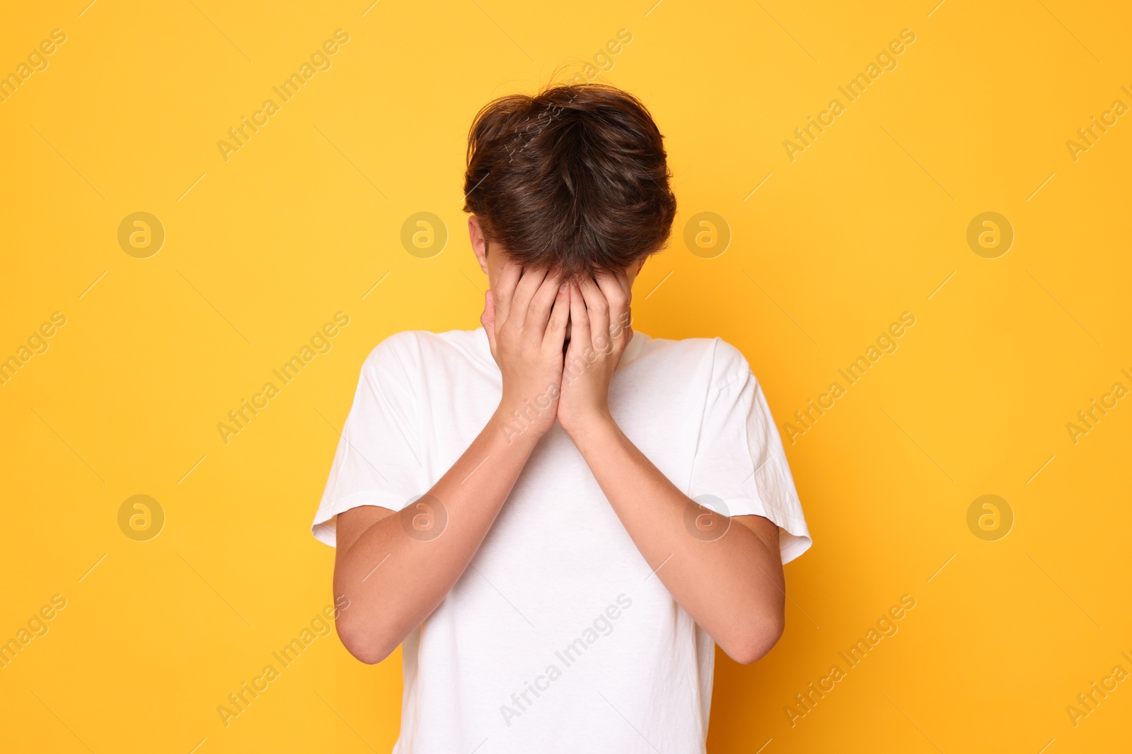 Photo of Scared teenage boy covering face with hands on orange background