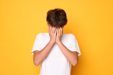 Photo of Scared teenage boy covering face with hands on orange background