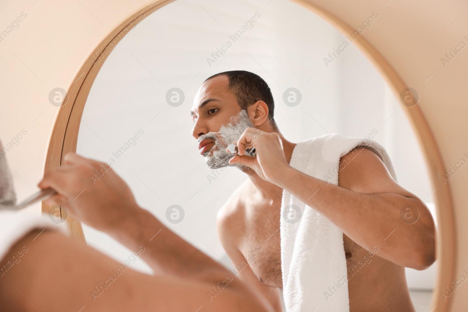 Photo of Handsome man shaving with razor near mirror in bathroom