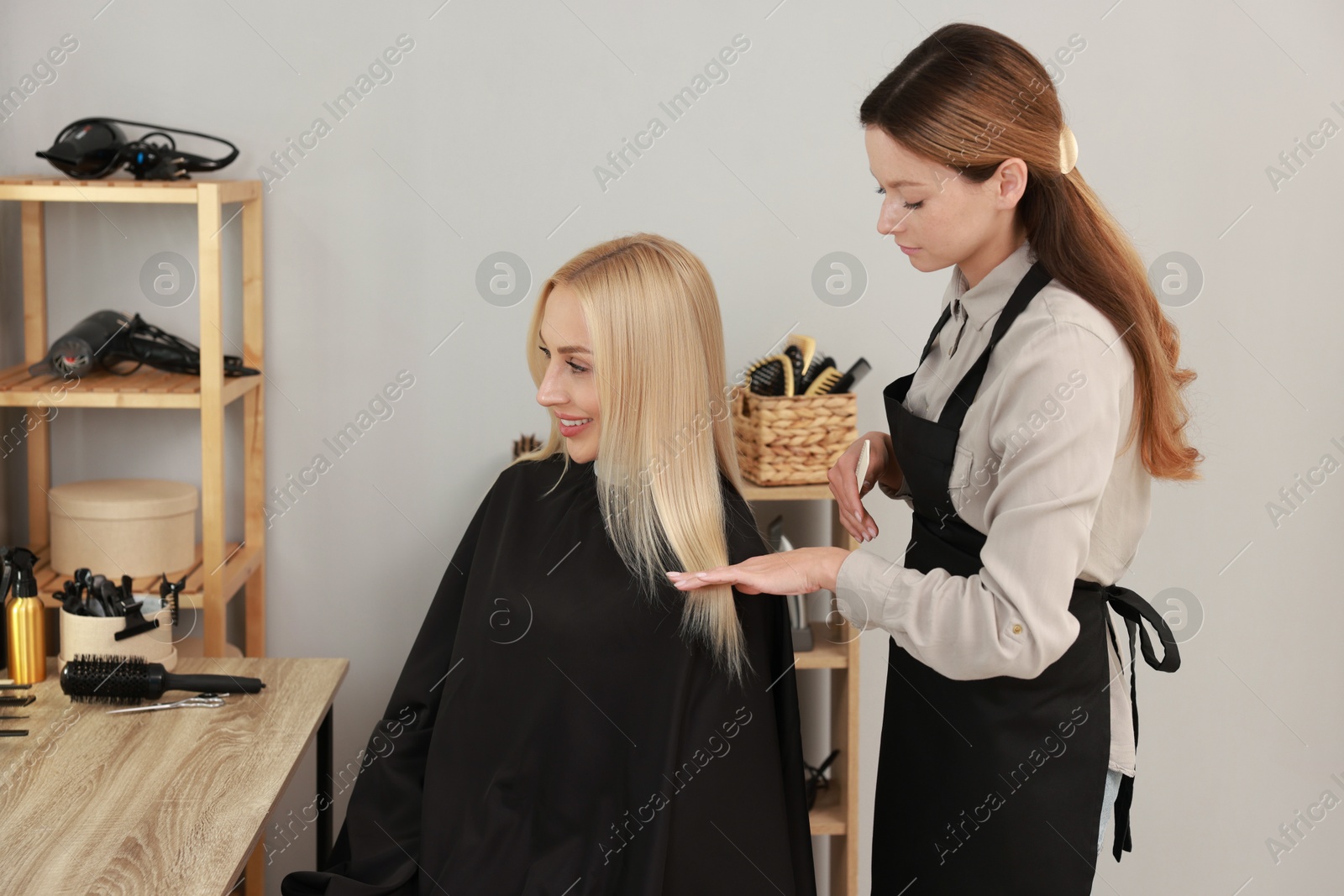 Photo of Professional hairdresser combing woman's hair in salon