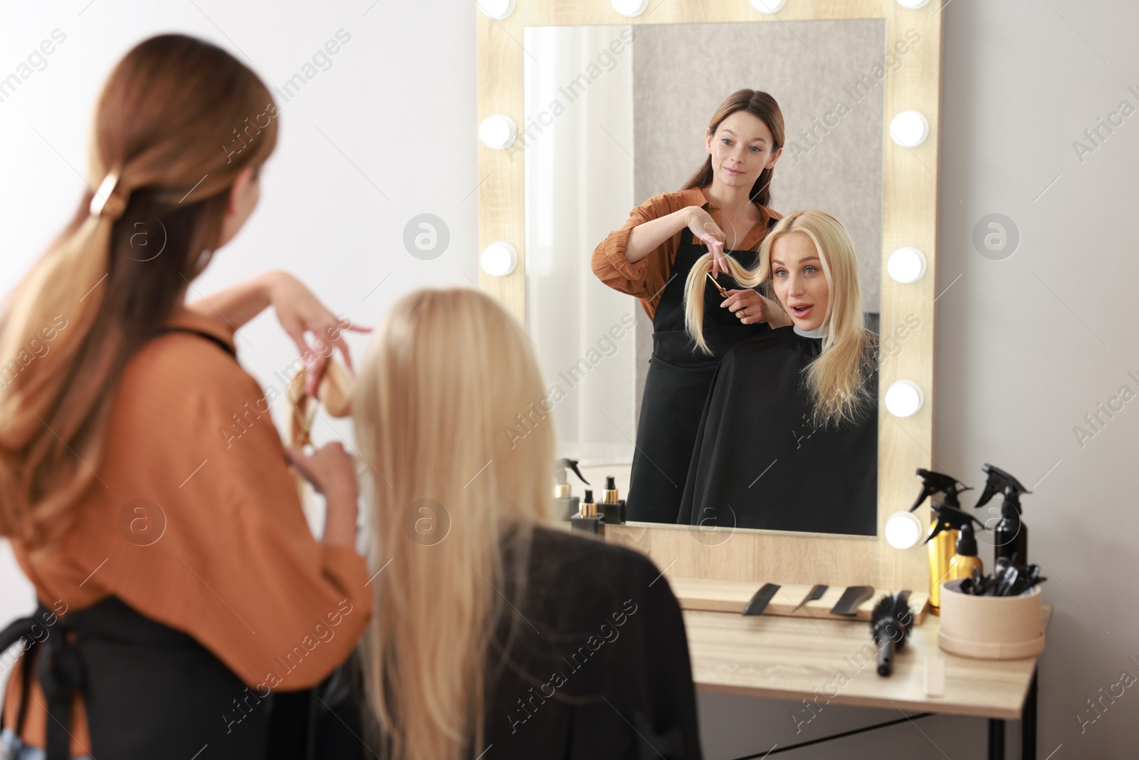 Photo of Hairdresser cutting client's hair with scissors in salon, selective focus