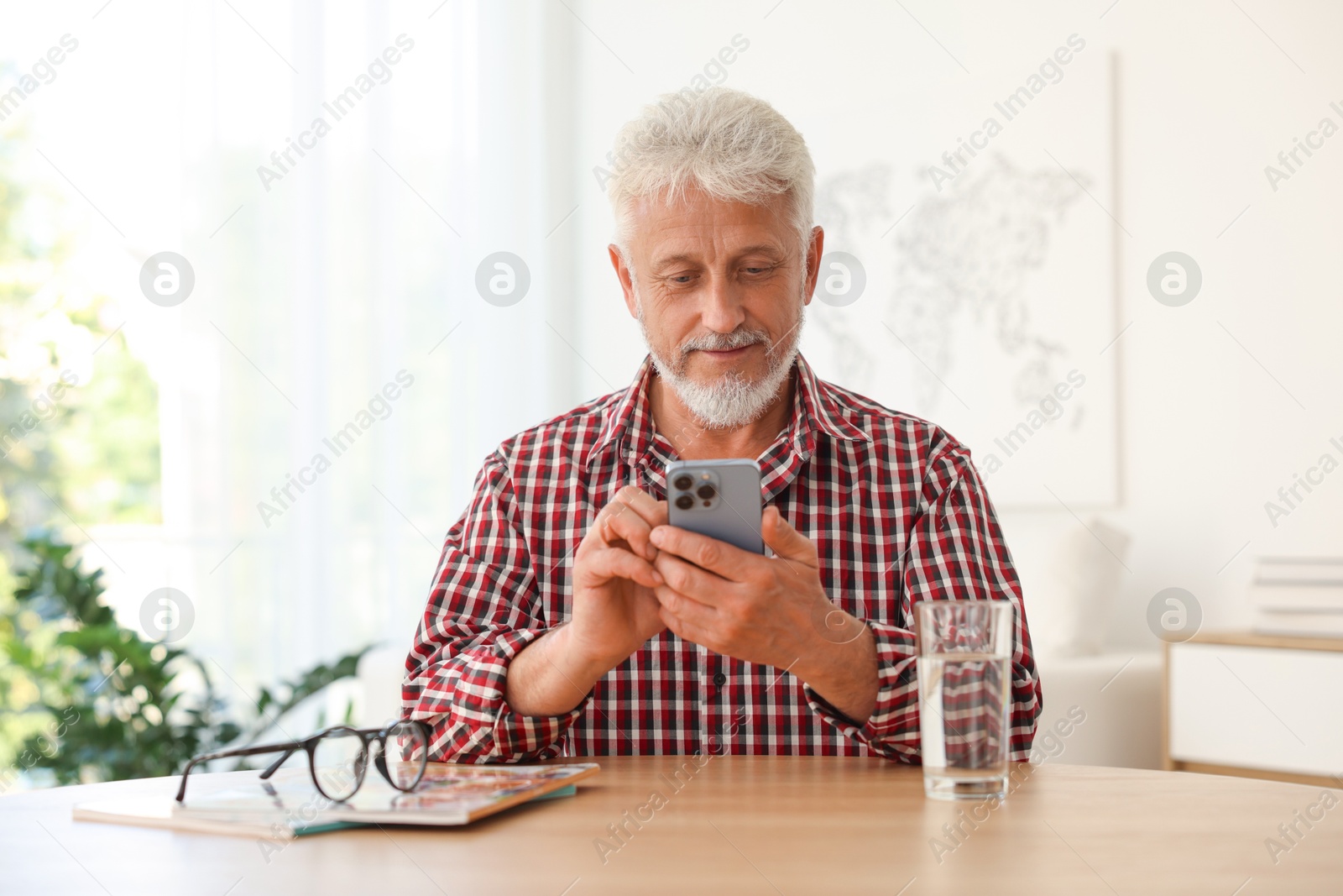 Photo of Senior man using smartphone at table indoors