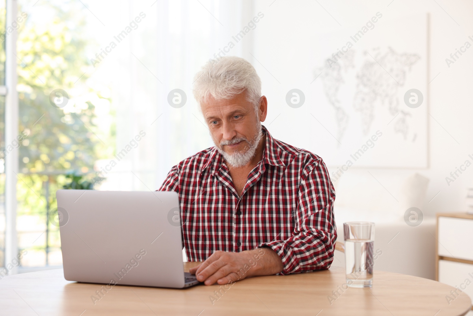 Photo of Senior man using laptop at table indoors